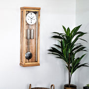 Ice Beech wooden wall clock by Hermle in living room scene on white wall next to potted plant.