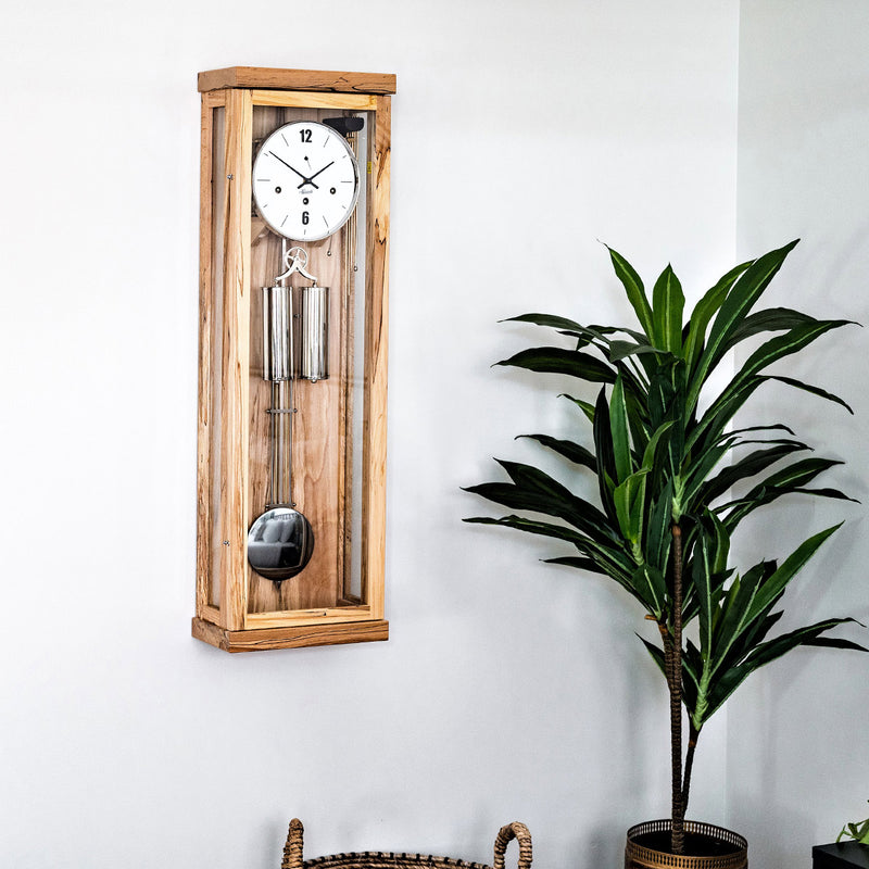 Ice Beech wooden wall clock by Hermle in living room scene on white wall next to potted plant.