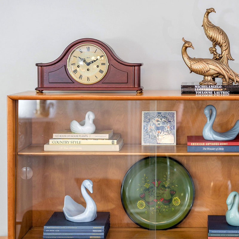 Wooden shelf with decorative items including a tambour style mantel clock, books, and bird figurines.
