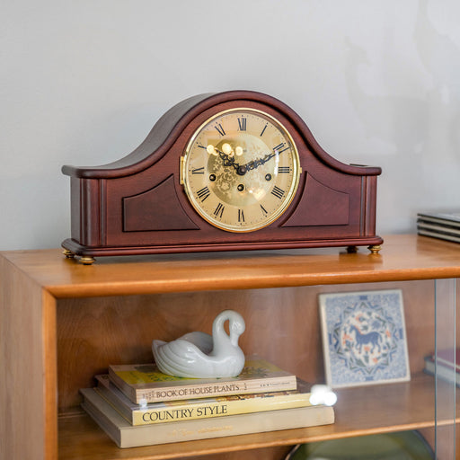 Wooden mantel clock on a shelf with books and decorative items.