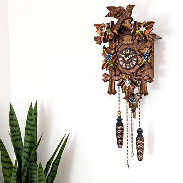 Wooden cuckoo clock with decorative elements on a white background with potted plant nearby