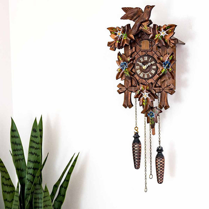 Wooden cuckoo clock with decorative elements on a white background with potted plant nearby