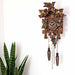 Wooden cuckoo clock with decorative elements on a white background with potted plant nearby
