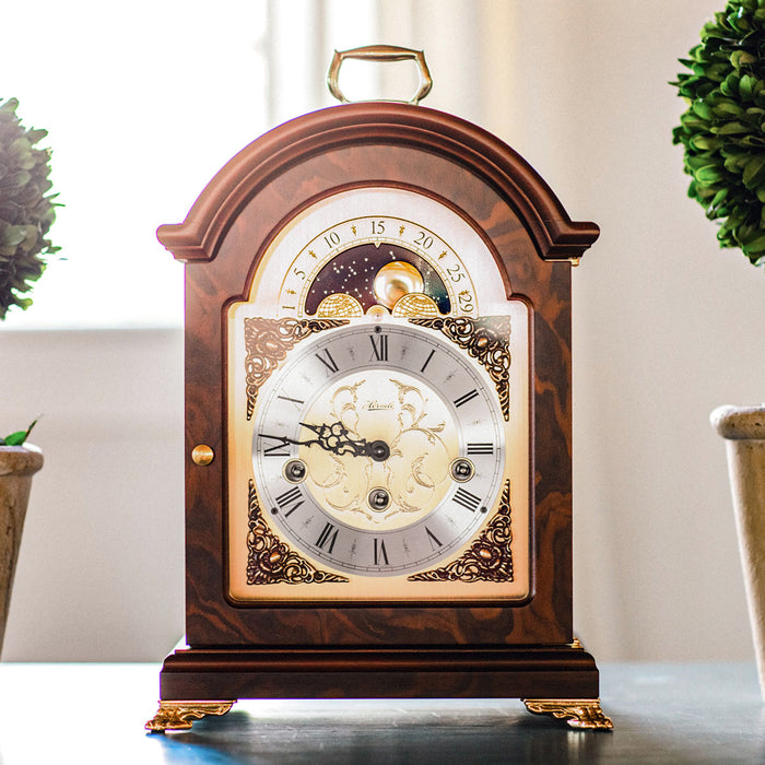 Decorative clock on table flanked by small trees with sunshine coming from window behind 