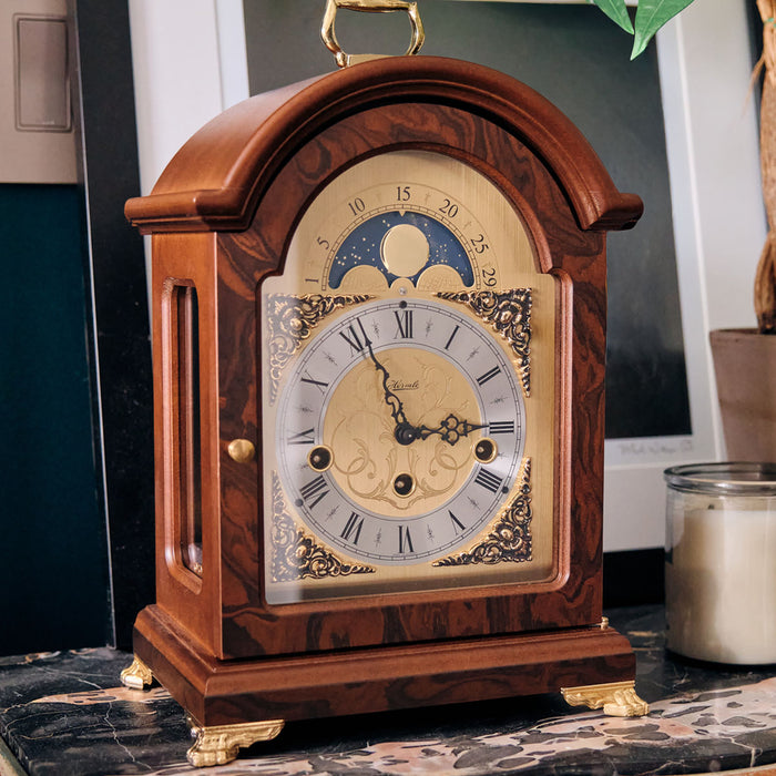 Decorative clock with gold highlights sitting on marble dresser with candle next to it