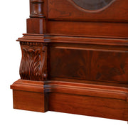Close-up of grandfather clock base made of ornately carved cherry wood on white background.