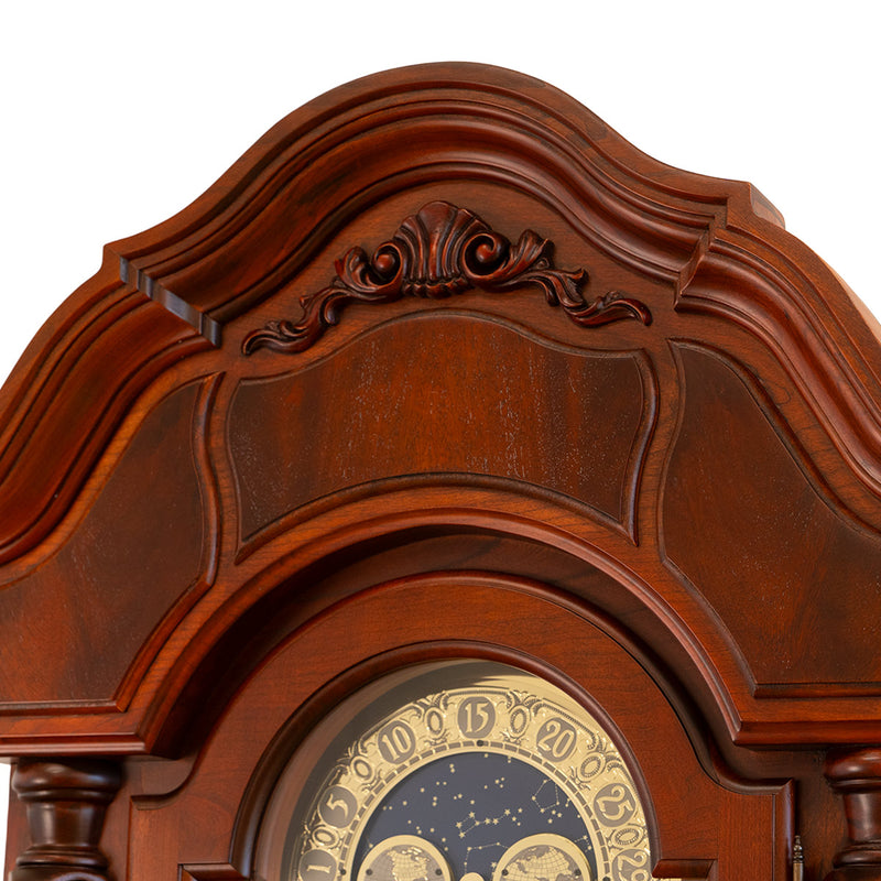 Close up of ornately carved grandfather clock crest made of cherry wood.