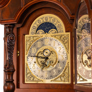 Close-up of brass clock face with ornate details on cherry wood grandfather clock.
