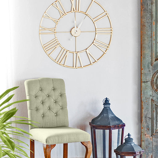 Decorative gold wall clock above a chair with a plant and lanterns in the foreground.