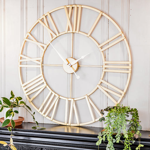 Large decorative wall clock with gold Roman numeral design on a white paneled wall.