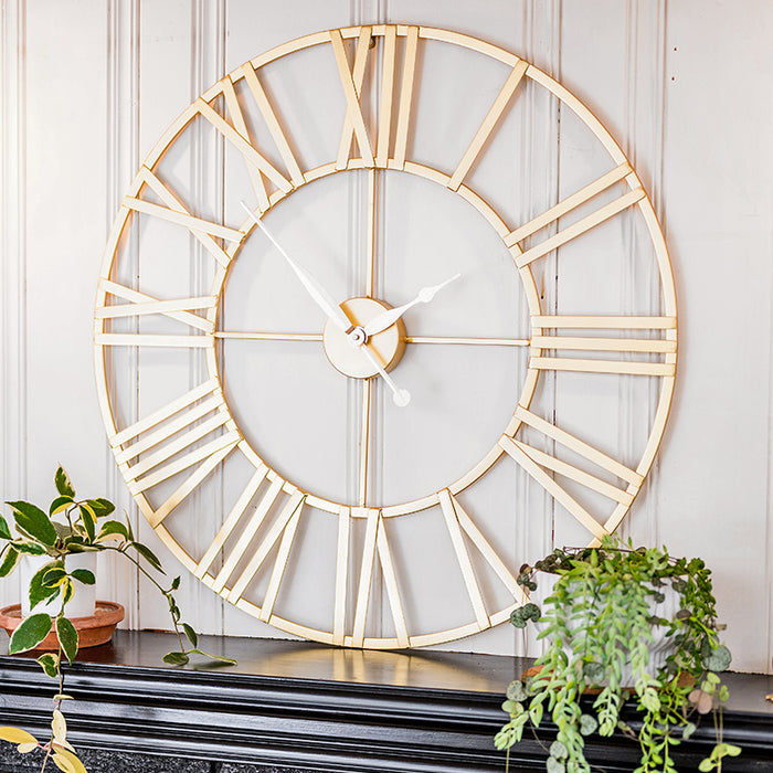 Large decorative wall clock with gold Roman numeral design on a white paneled wall.