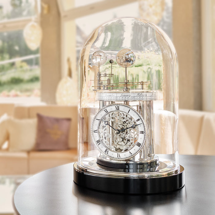 Black mechanical clock under a glass dome on a table with a blurred indoor background