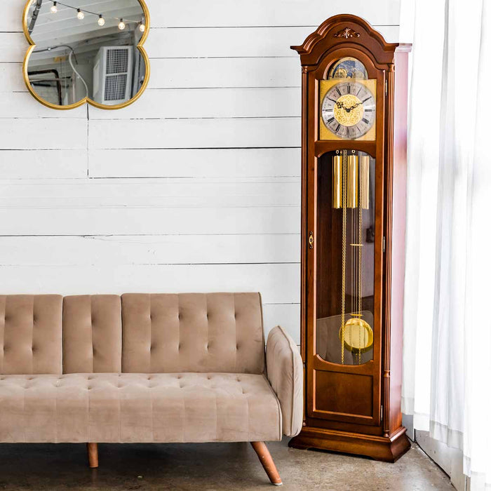 Wooden grandfather clock next to a beige sofa in a room with white walls.