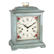Blue decorative clock with floral design and holes on the face for winding on a white background