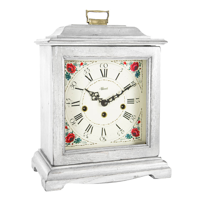 White decorative clock with floral design and holes on the face for winding on a white background