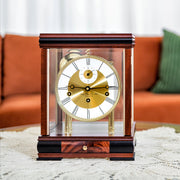Dark mahogany mantel clock with brass face on living room table with couch in background.