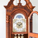 Ornate wooden grandfather clock with detailed face against white wall