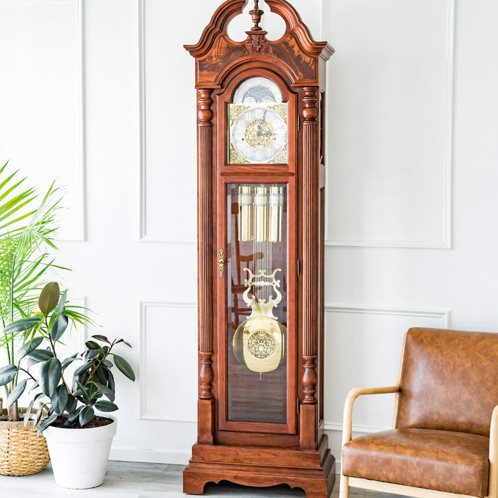 Cherry wood grandfather clock in white room with a green plants and leather chair.