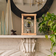 Light wood mantel clock on marble mantel next to green plant