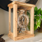 Light wood mantel clock on marble tabletop next to green plant.