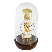 Walnut Mechanical clock with glass dome and visible brass gears and roman numeral face on white background.