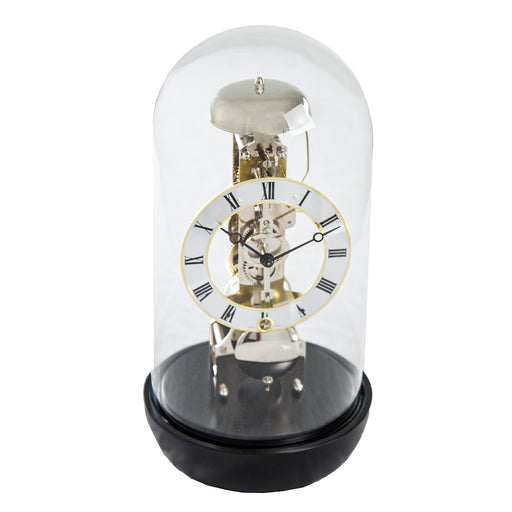 Black Mechanical clock with glass dome and visible nickel gears and roman numeral face on white background.