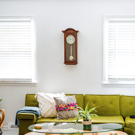Cherry wood wall clock hanging above green sofa on white wall