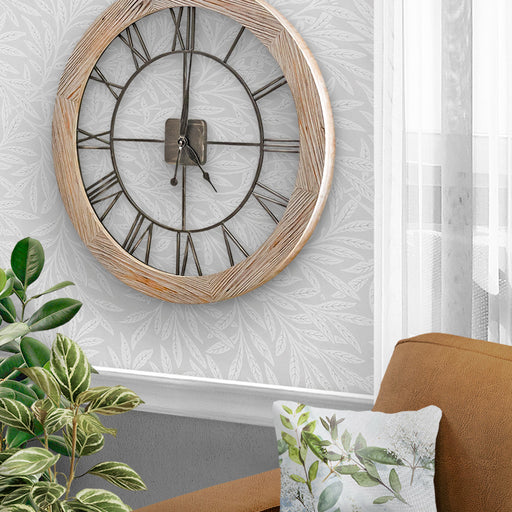 Farmhouse style round wooden wall clock with metal face, in a room with a plant and sofa.