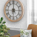 Farmhouse style round wooden wall clock with metal face, in a room with a plant and sofa.