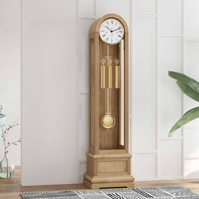Oak grandfather clock in front of white wall with plants at the edges of the room 