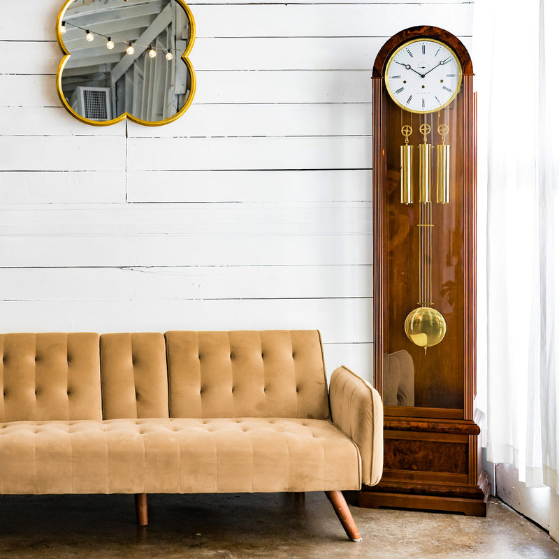 Walnut grandfather clock in front of white plank wall, next to beige couch 