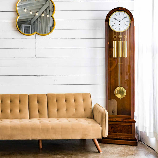 Walnut grandfather clock in front of white plank wall, next to beige couch 