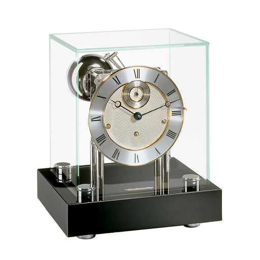 Black desk clock with glass case and nickel clock face with brass highlights on white background