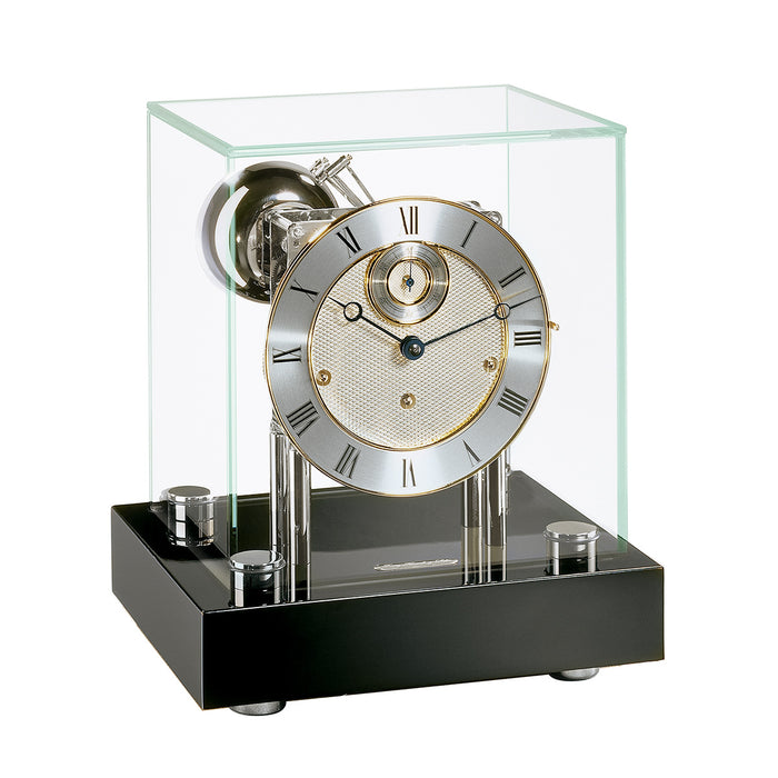 Black desk clock with glass case and nickel clock face with brass highlights on white background