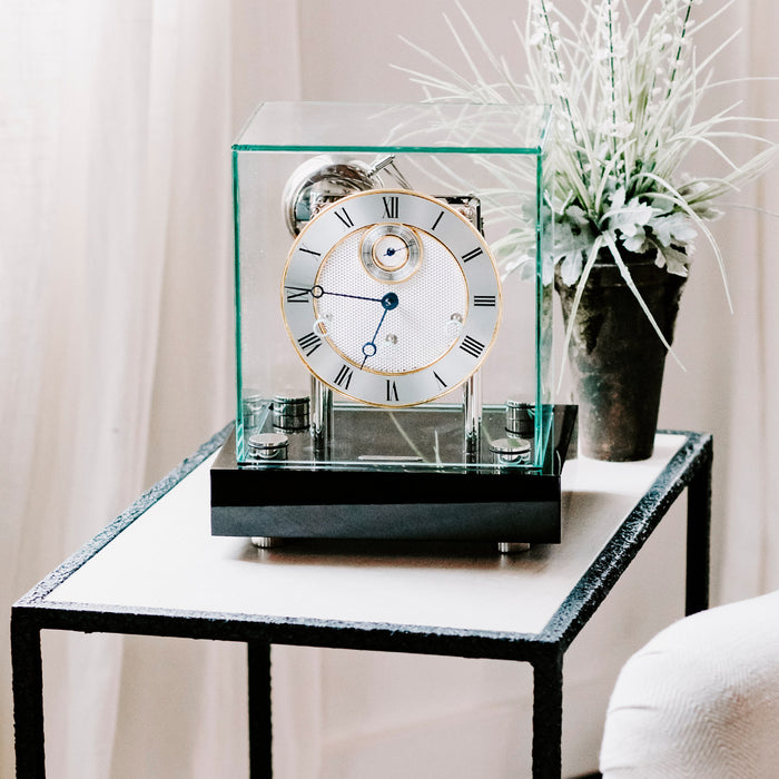 Black desk clock with glass case sitting on black and white side table in white room 