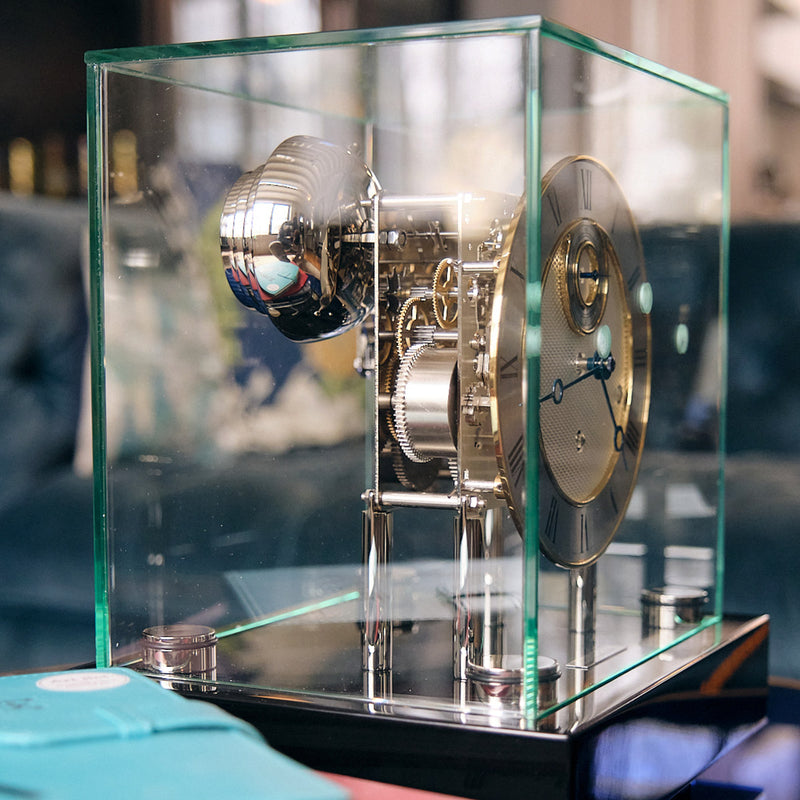 Intricate nickel gears and bell inside glass case of black desk clock 