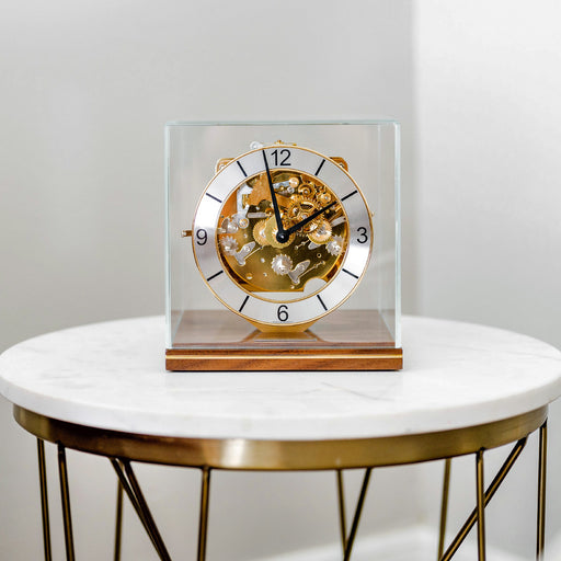 Decorative clock with mechanical gears on a walnut base on a white marble table.