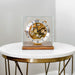 Decorative clock with mechanical gears on a walnut base on a white marble table.
