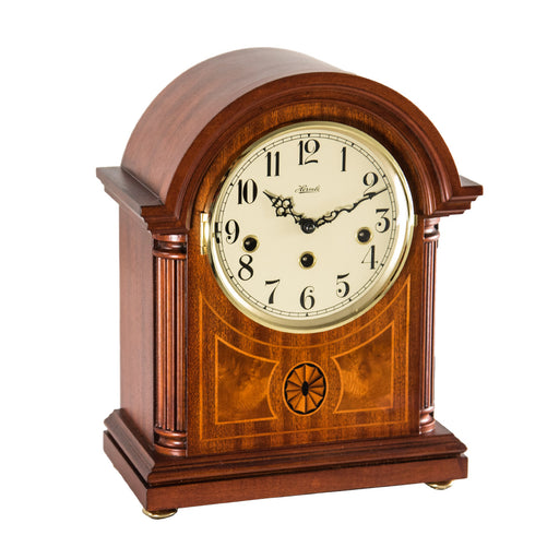Wooden mantel clock with holes for winding the mechanical movement inside on white backdrop