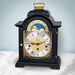 Black and brass clock on marble shelf in front of pale blue wall 