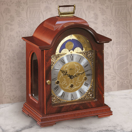 Mahogany and brass clock on white marble shelf in bedroom with tan wallpaper
