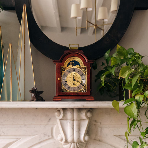 Mahogany and brass clock on a marble mantelpiece with plants and a mirror in the background
