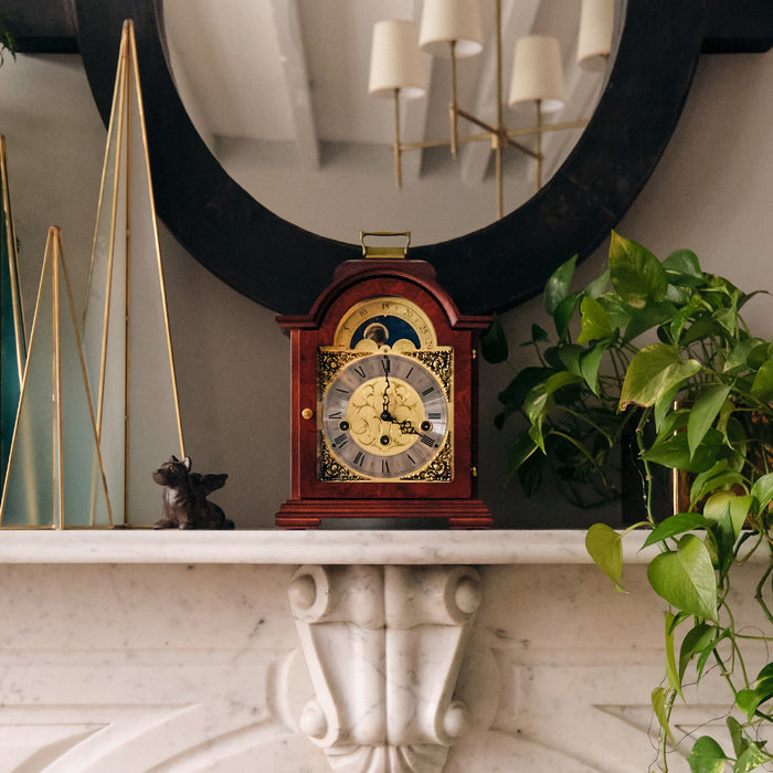 Mahogany and brass clock on a marble mantelpiece with plants and a mirror in the background