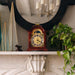 Mahogany and brass clock on a marble mantelpiece with plants and a mirror in the background
