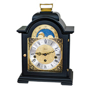 Black and brass mantel clock with roman numerals and ornate face on white background.