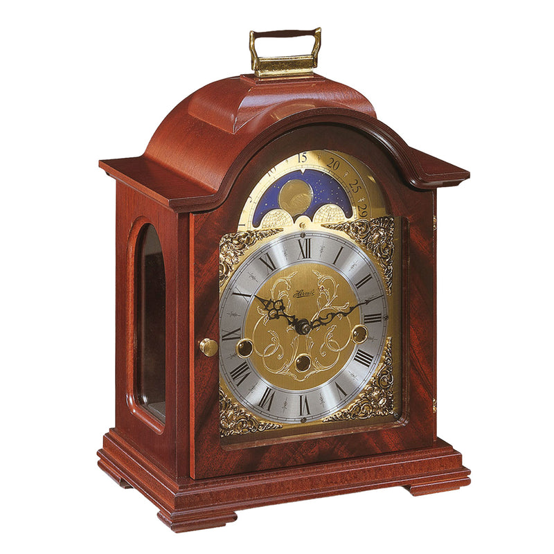 Mahogany wood and brass mantel clock with roman numerals and ornate face on white background.