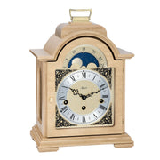 Oak wood and brass mantel clock with roman numerals and ornate face on white background.