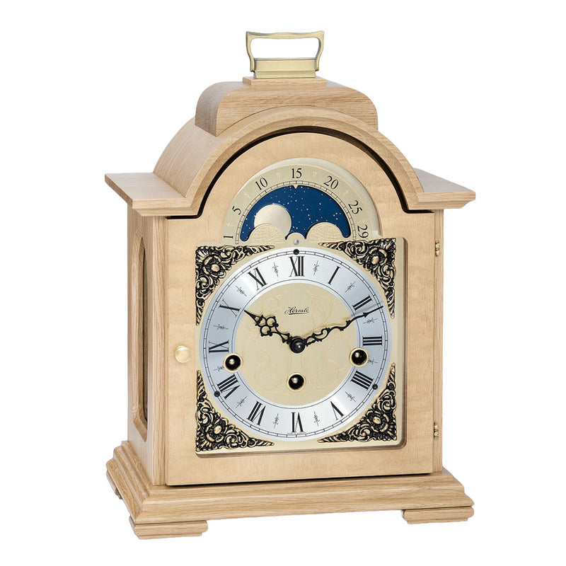 Oak wood and brass mantel clock with roman numerals and ornate face on white background.