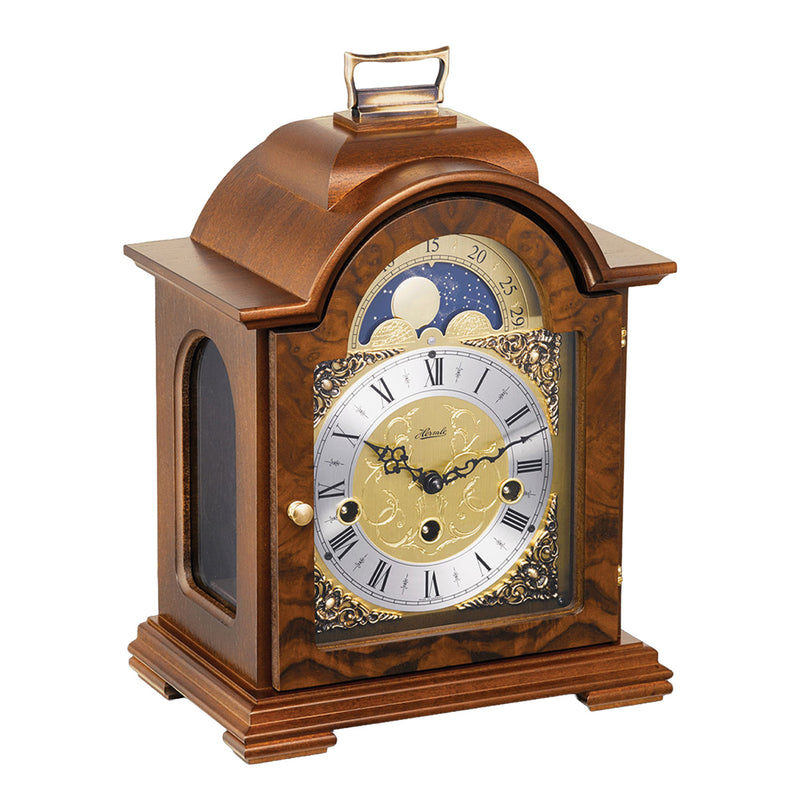 Walnut wood and brass mantel clock with roman numerals and ornate face on white background.