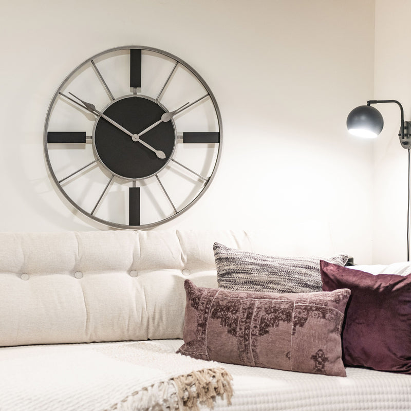 Black and metal wall clock with silver hands hanging above white couch in living room.